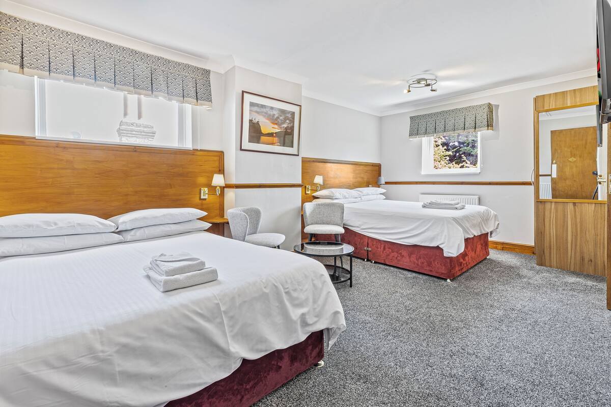 A hotel room with two beds, a small table, and a chair.