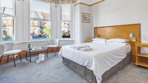 Camera d'albergo con un letto grande, un tavolino con un bollitore, una sedia e una finestra con tende.