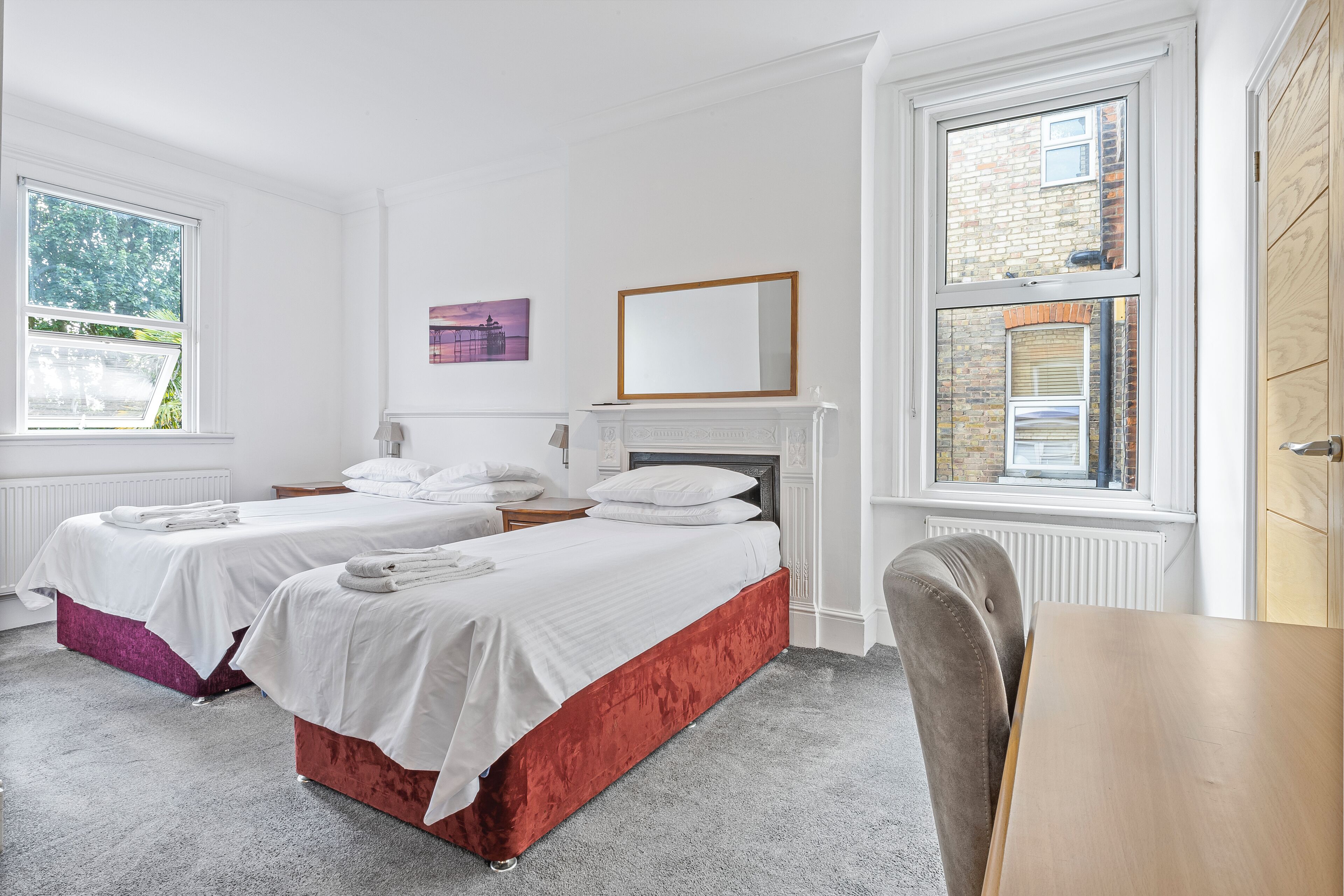 A hotel room with two beds, a wooden table, a chair, and a fireplace.