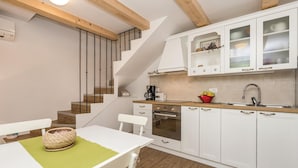 Una cocina moderna con armarios blancos, una escalera de madera y un comedor con camino de mesa verde.