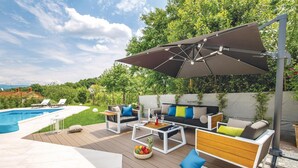 Un patio exterior con piscina, terraza de madera y zona de estar con mesa y sillas.