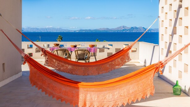 Una hamaca en un balcón con vista al mar y a las montañas.