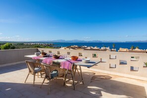 A terrace with a table set for dining, overlooking a coastal landscape with mountains in the distance.