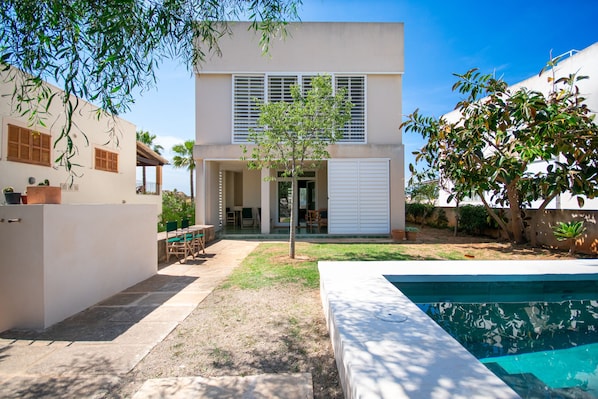A modern two-story house with a covered patio, a swimming pool, and a small tree in the yard.