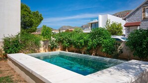 Una piscina rectangular con superficie de agua azul cristalina, rodeada por un bajo muro de piedra y abundante follaje verde.