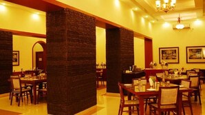 Un restaurante con varias mesas y sillas, pilares de ladrillo y cuadros en las paredes.