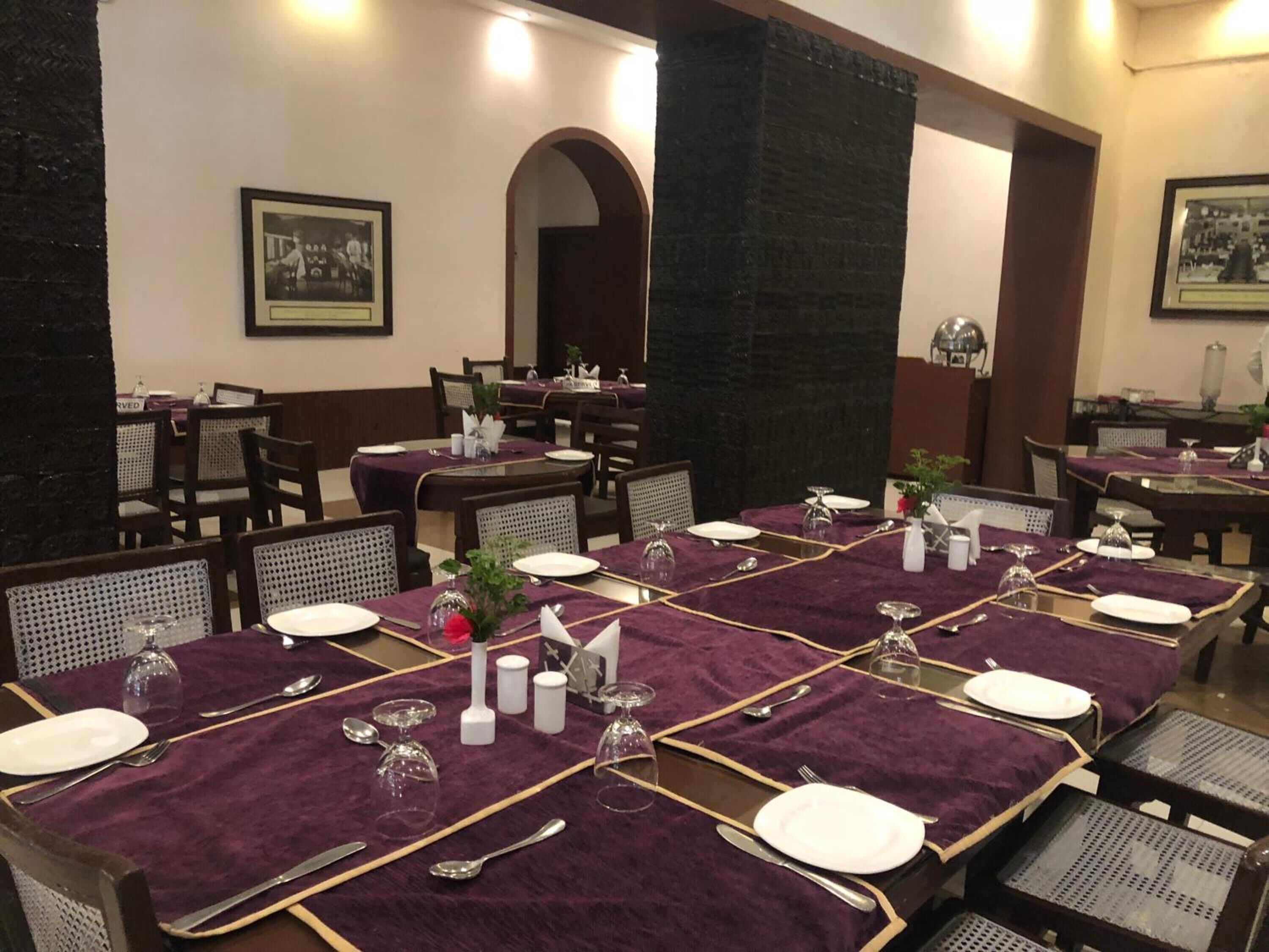 A dining area with tables set for four, featuring purple tablecloths, white plates, and silverware.