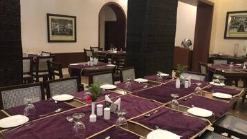A dining area with tables set for four, featuring purple tablecloths, white plates, and silverware.