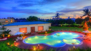 Una piscina con diseño en forma de corazón, rodeada por un jardín ajardinado y un edificio con tejado azul.