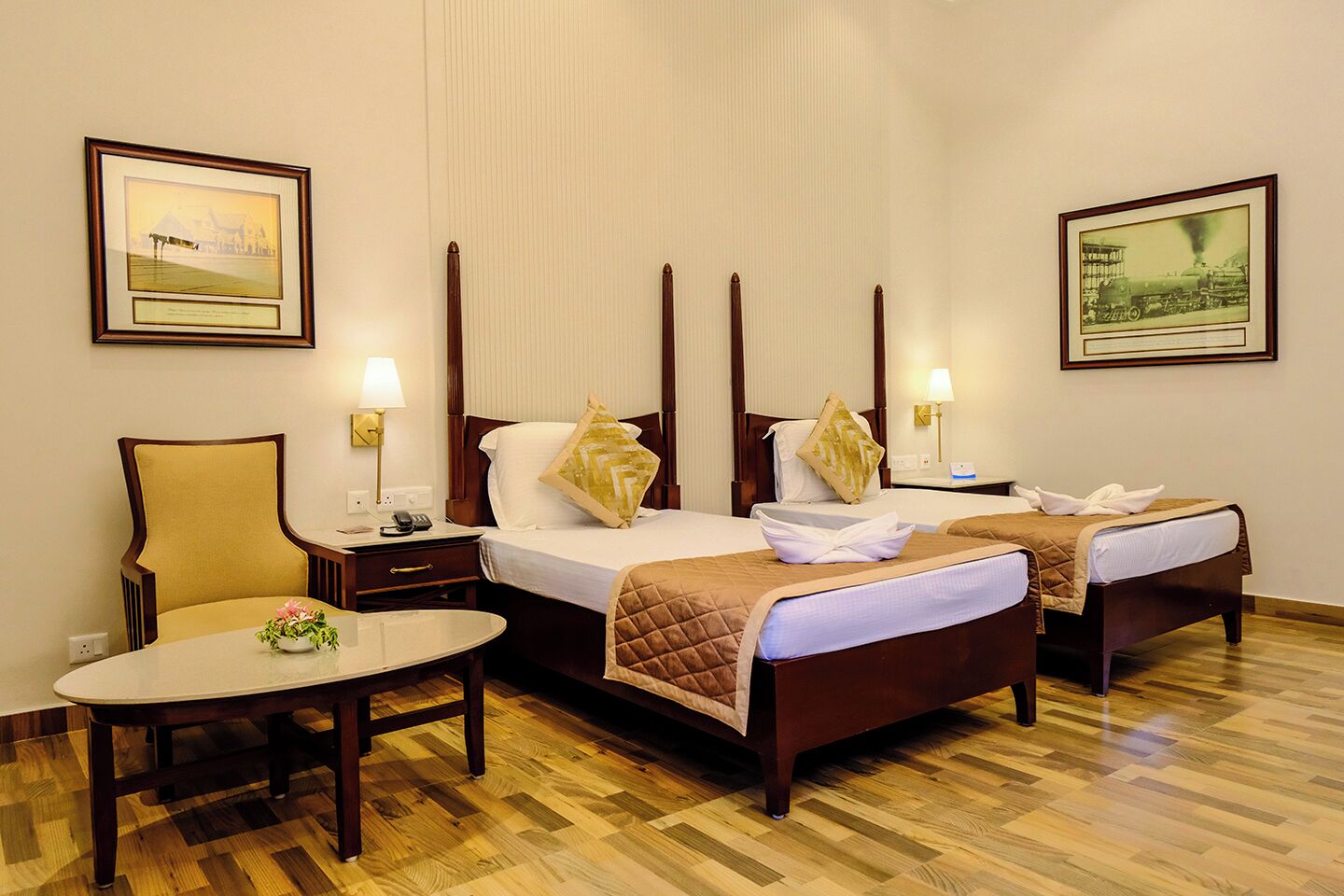 A hotel room with two beds, a chair, a table, and two framed pictures on the walls.
