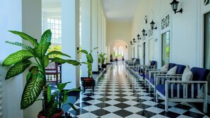 Un pasillo de hotel con piso a cuadros, plantas en macetas, rincones de estar y lámparas fijadas a la pared.