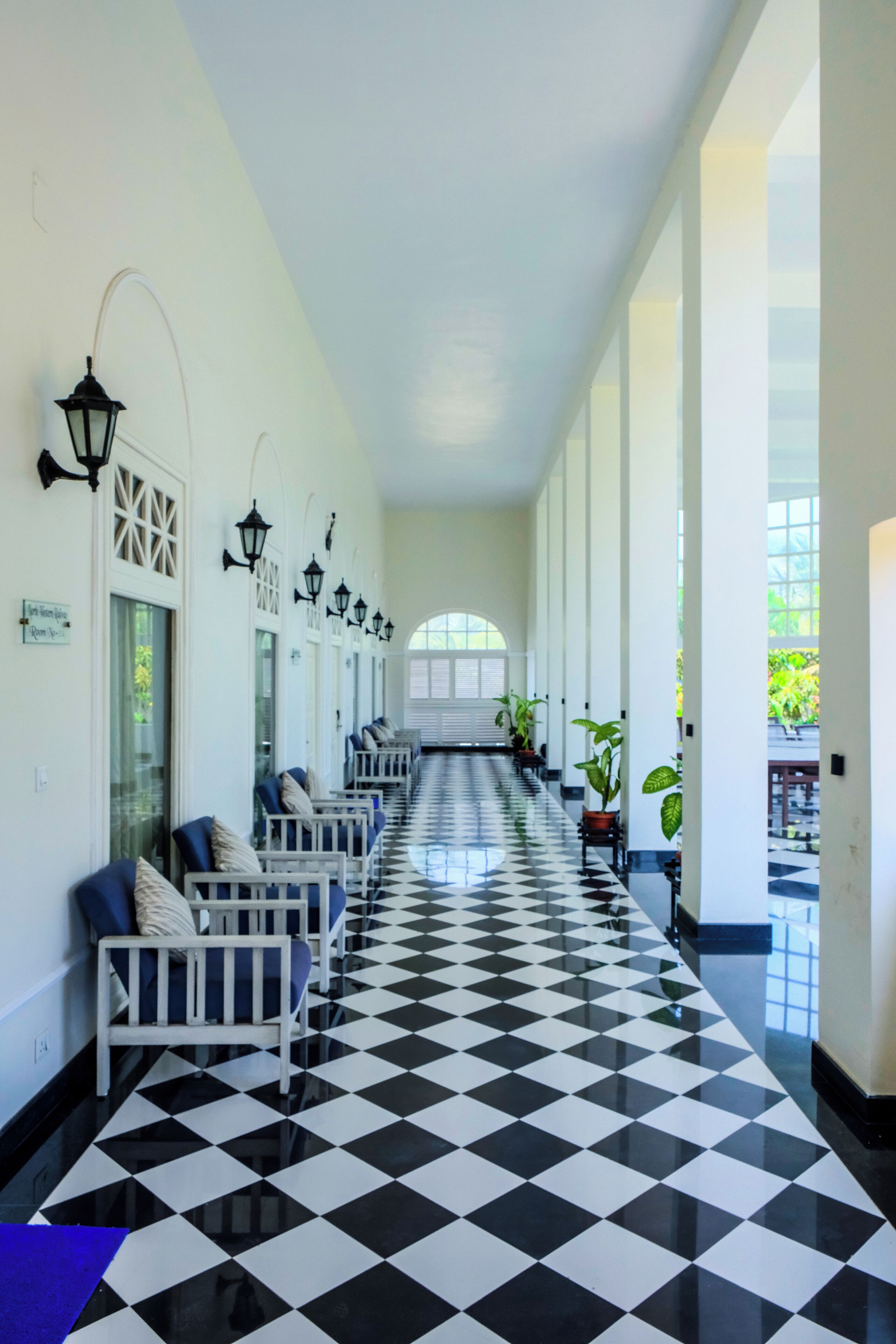 A long corridor with a checkered floor, white walls, and black lamps.