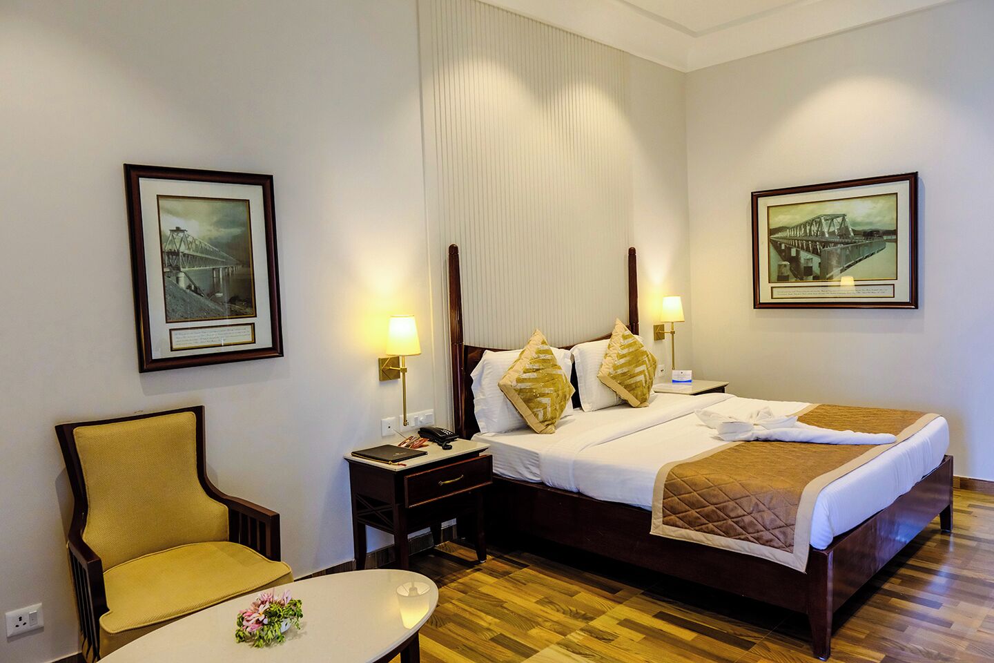 A hotel room with a bed, bedside tables, a chair, and two framed pictures on the walls.