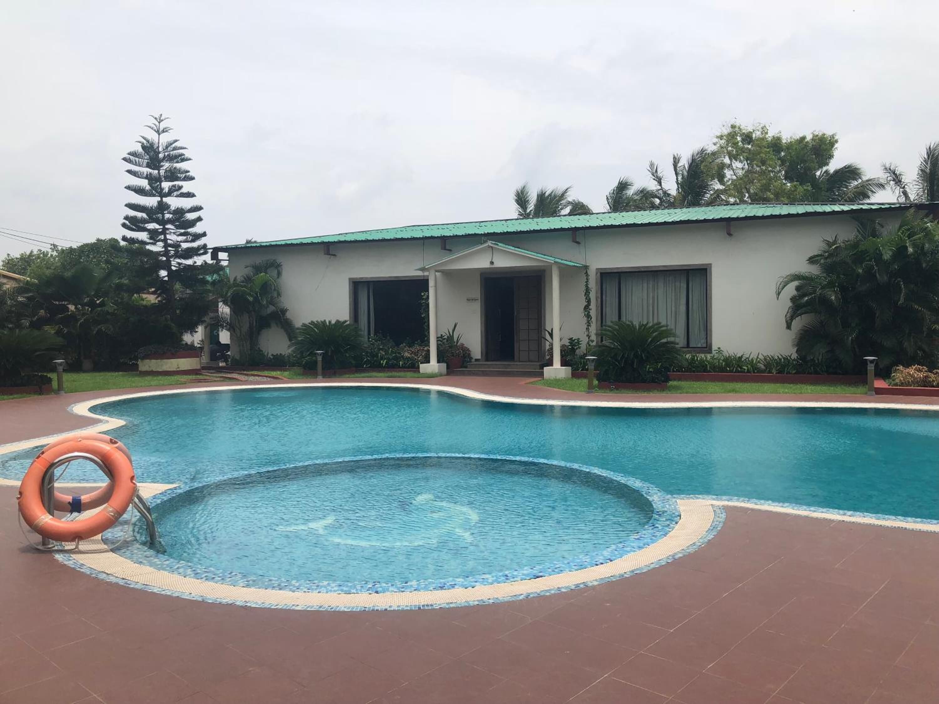 Una piscina con un flotador salvavidas, rodeada por un edificio de techo verde y entrada cubierta.