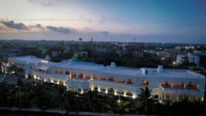 Un hotel grande de varios pisos con un patio central, rodeado de palmeras y otros edificios.
