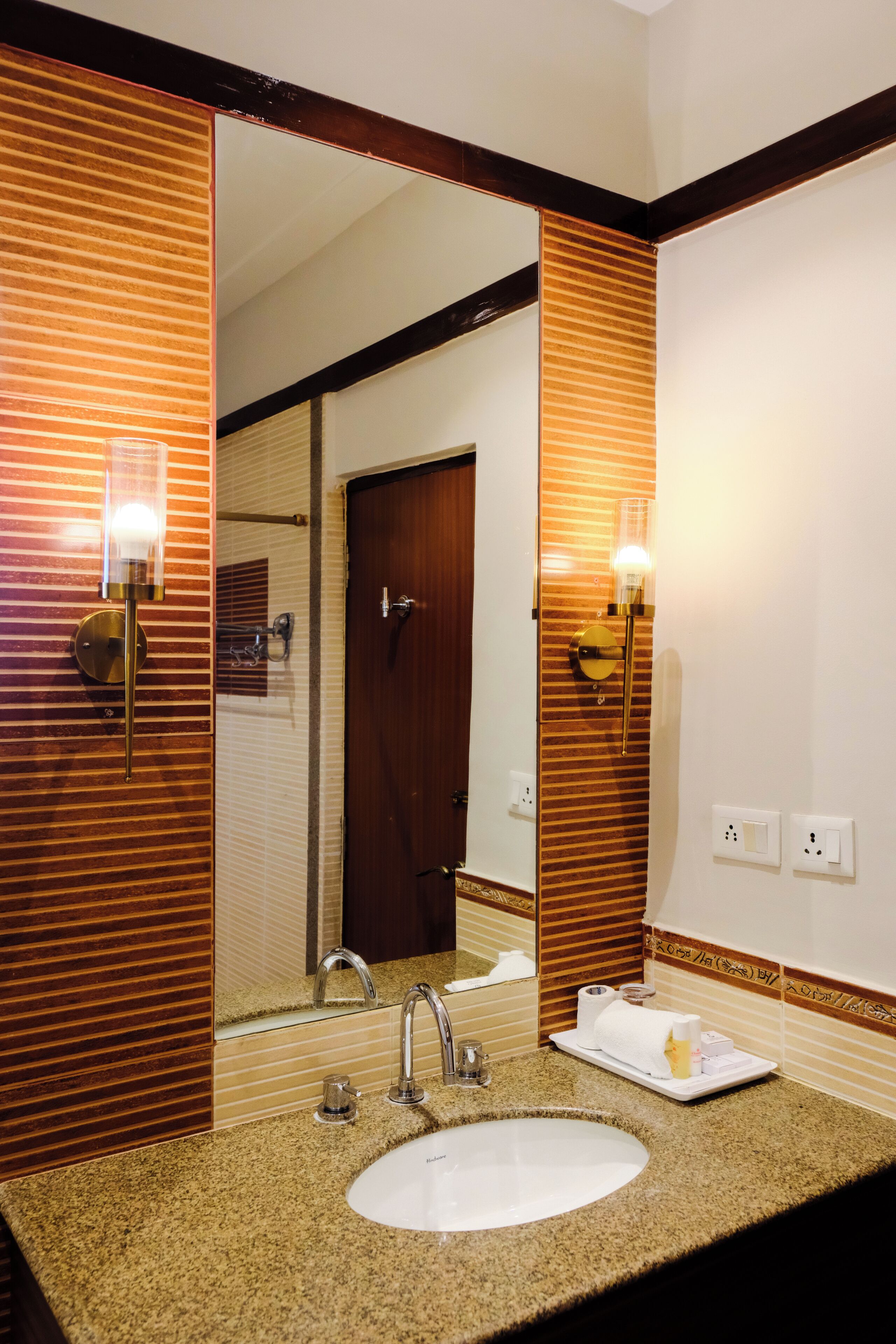 Une salle de bain d’hôtel avec un grand miroir, un lavabo et deux appliques murales.