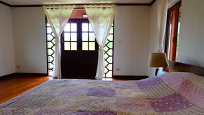 A bedroom with a large bed, a wooden floor, a window with a lattice design, and a lamp on a nightstand. - Villa Franjipani Maerim (Mae Rim)