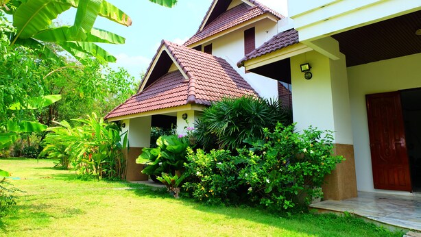 A two-story building with a tiled roof, surrounded by lush greenery and a well-maintained lawn. - Villa Franjipani Maerim (Mae Rim)