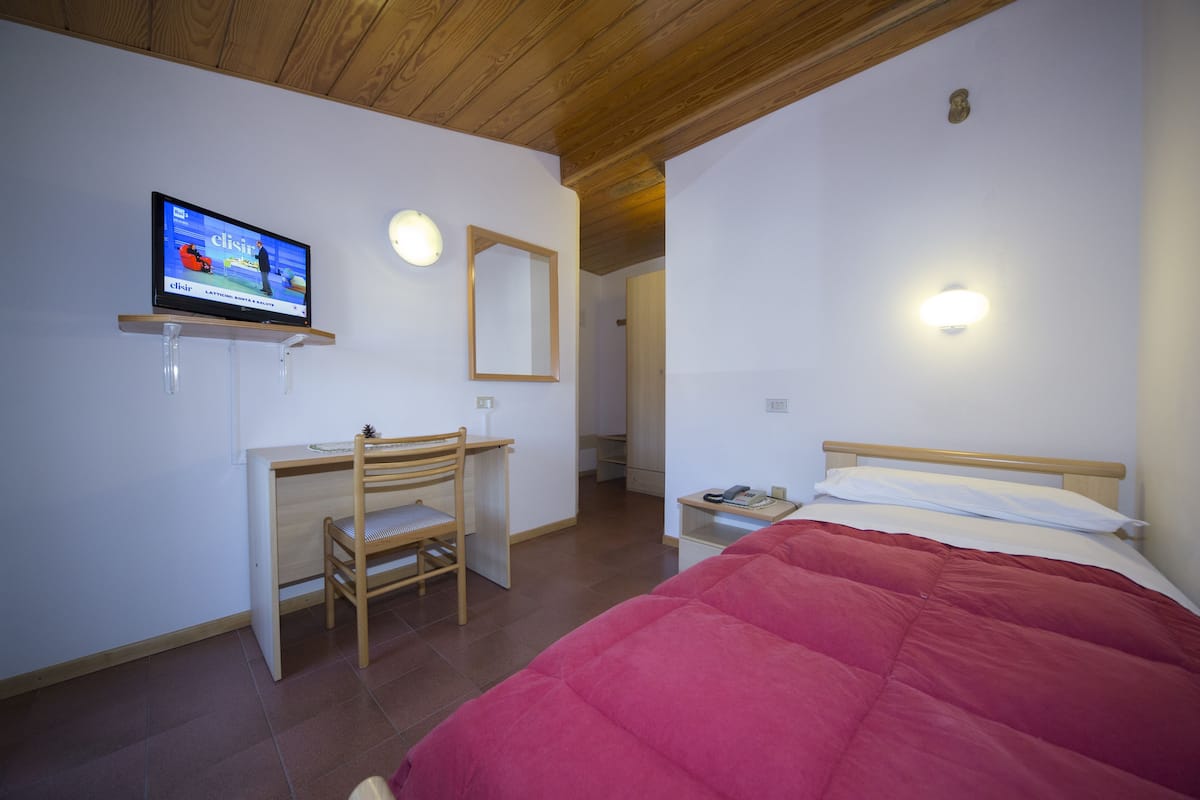 A bedroom with a bed, a desk with a chair, a television, and a mirror.