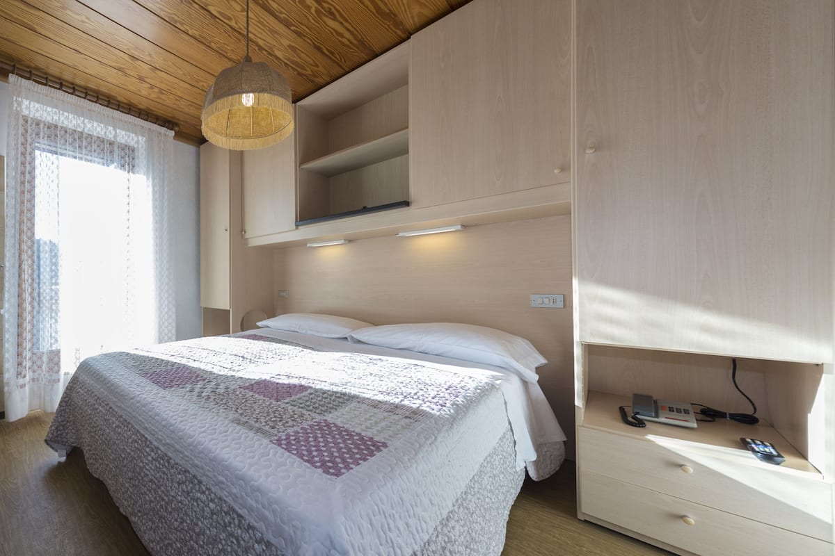 A bedroom with a bed, a bedside table with a phone and charger, and built-in shelving.