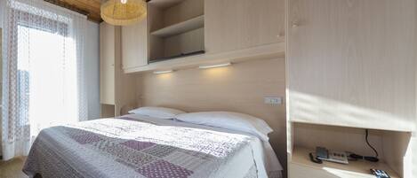 Un dormitorio con cama, mesita de noche con teléfono y cargador, y estanterías empotradas.