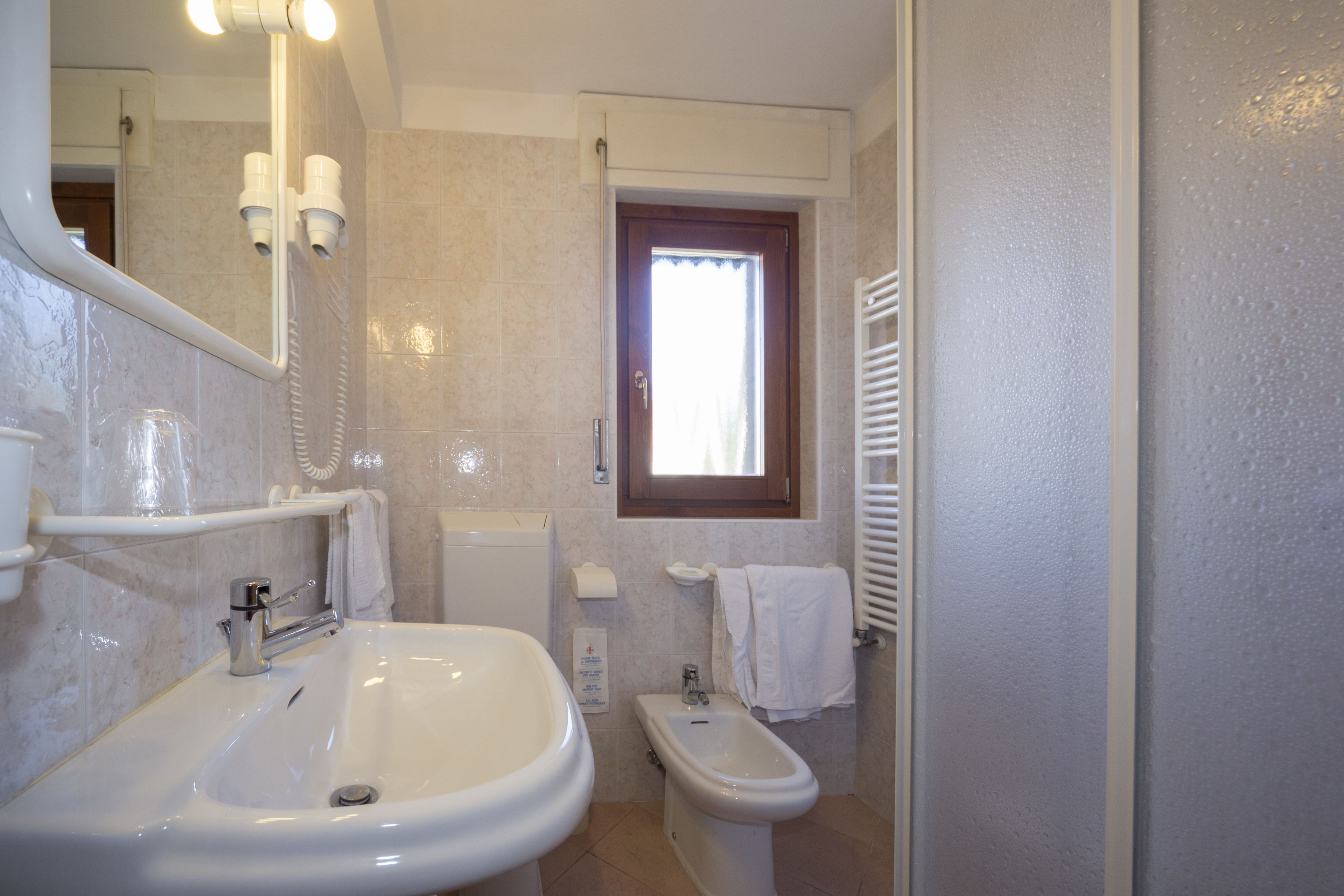 A bathroom with a sink, bidet, mirror, towel rack, and window.