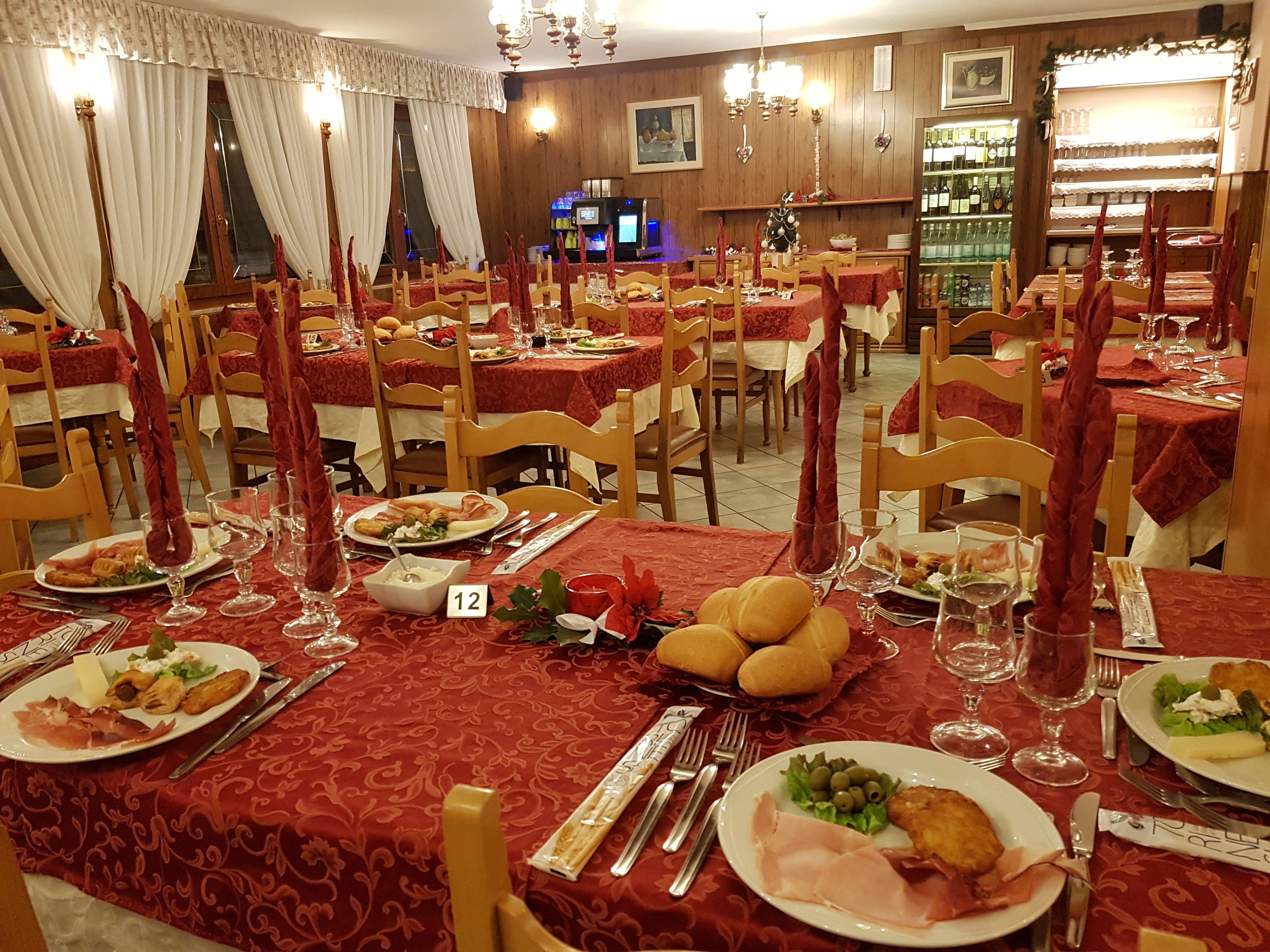 Un ristorante con diversi tavoli apparecchiati per consumare all'interno, ognuno con tovaglie rosse e candele.