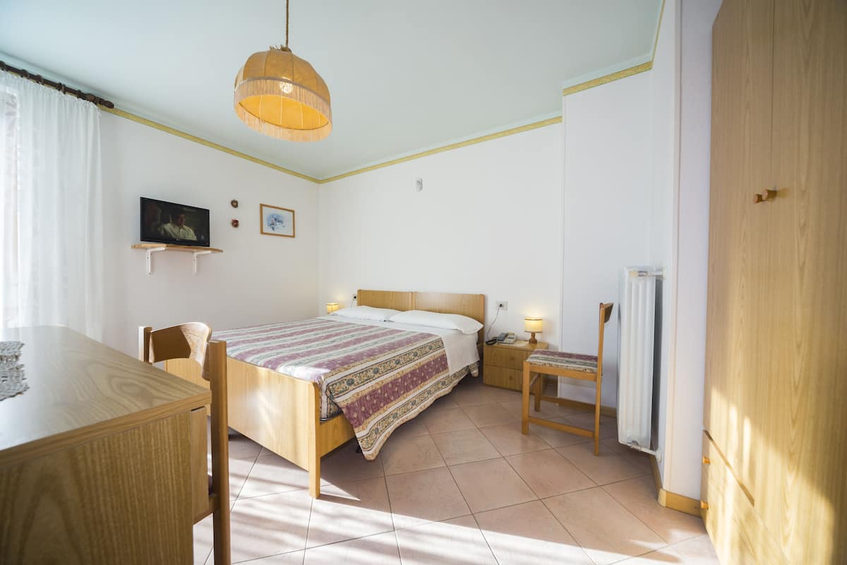 A bedroom with a bed, bedside table, lamp, and a television on a stand.