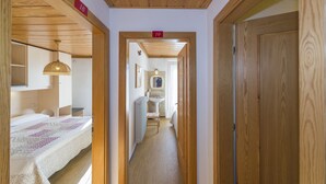 Passadís estret amb parets i portes de fusta, que condueix a un bany amb rentapla i mirall.