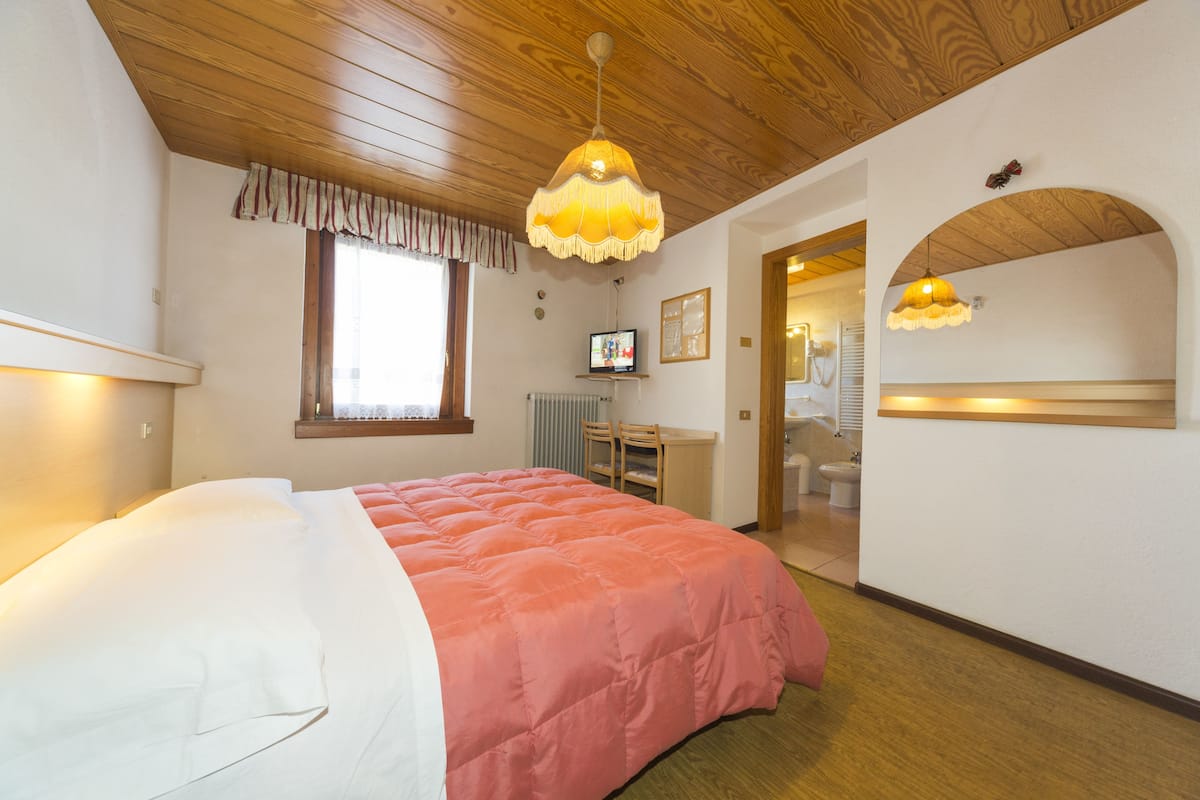 A bedroom with a bed, a television, a desk, and a bathroom visible through an archway.