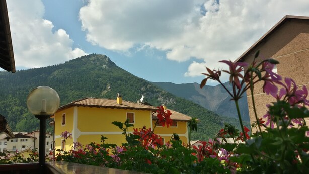 Un edifici groc amb teules vermelles, envoltat de vegetació abundant i muntanyes al fons.
