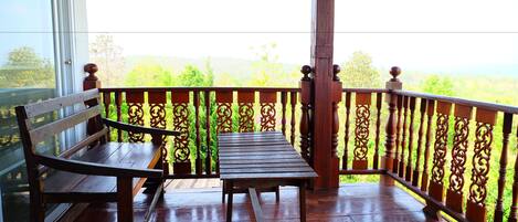 A wooden deck with a bench and table, surrounded by ornate railings, overlooking a lush landscape.