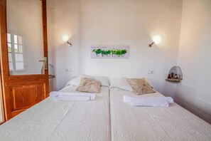 A double room with two beds, each with a white bedspread and pillows, a wooden door, and a wall-mounted light fixture. - 44246 Finca Sa Cova, Spain (Petra)