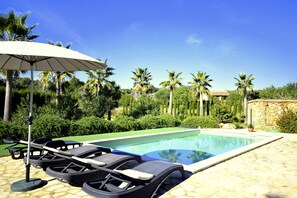 A poolside area with lounge chairs and an umbrella, surrounded by palm trees and greenery. - 44246 Finca Sa Cova, Spain (Petra)