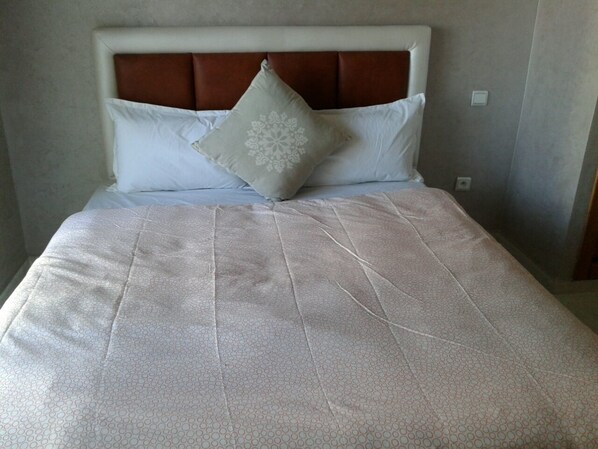 A bed with a patterned bedspread, a headboard, and two pillows.