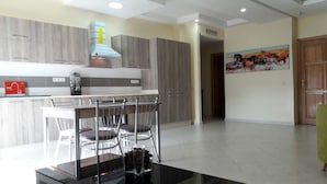 A modern kitchen with grey cabinets, a black countertop, and a dining area with a glass table and metal chairs.