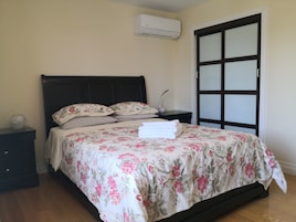 Een slaapkamer met een bed, nachtkastje, airconditioning en een schuifdeur.