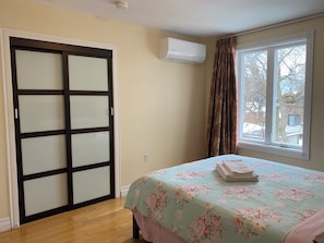 Un dormitorio con cama, ventana con cortinas, aire acondicionado de pared y puerta corrediza.