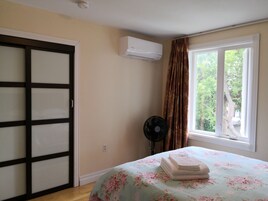 Een slaapkamer met een bed, een raam met gordijnen, een airconditioner en een ventilator.