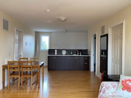 Een ruime woonkamer met een houten eettafel en stoelen, een keuken met donkere kastjes, en een groot raam.