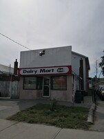 Een Dairy Mart winkel met een rood-wit bord, een bakstenen schoorsteen en een klein tuintje ervoor.