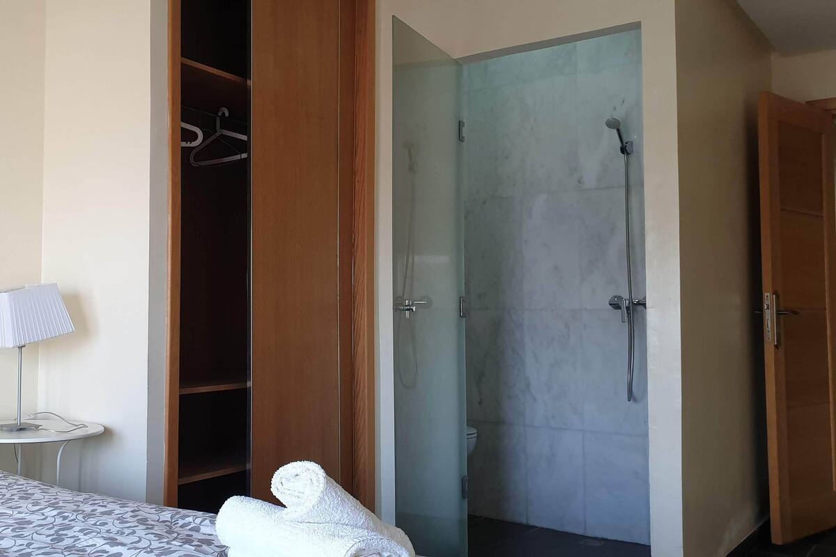Ein Hotelzimmer mit Bett, Nachttisch mit Lampe, Kleiderschrank und Duschbereich.