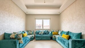 A living room with a teal sofa set, a large window, and a tiled floor.