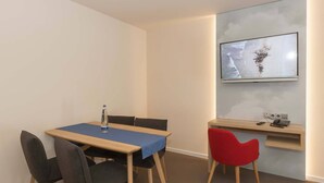 A modern room with a wooden table and chairs, a blue tablecloth, a red chair, a mounted TV, and a small shelf with a phone and remote. - Dachappartement (Berchtesgaden)