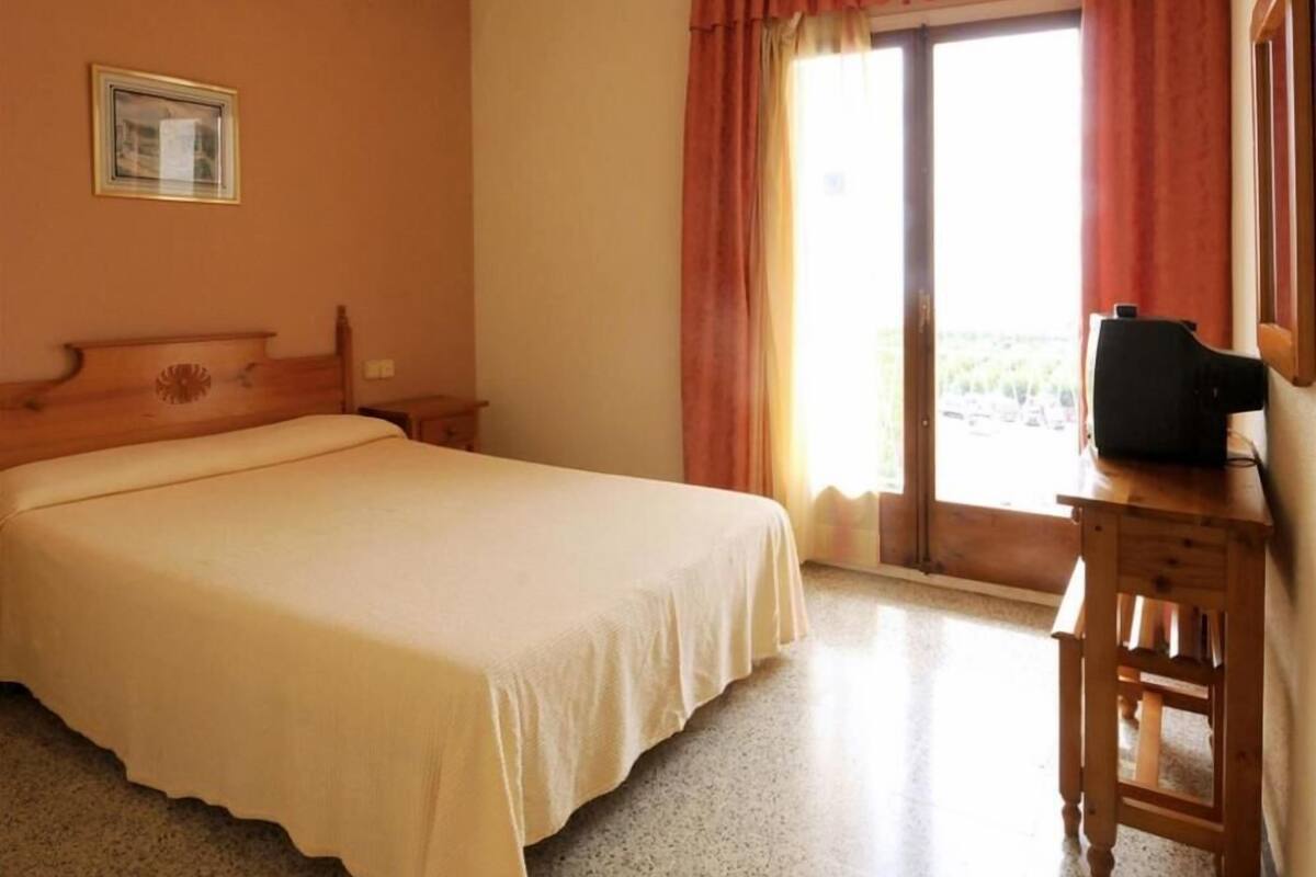Een hotelkamer met een groot bed, een houten nachtkastje, een televisie en een raam met gordijnen.