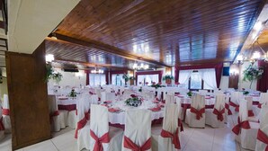 Une salle de banquet avec des tables rondes, des nappes blanches et des rubans rouges sur les chaises.