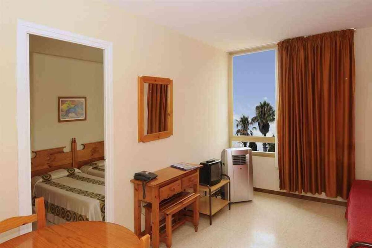 Een hotelkamer met een bed, een bureau met een computer, een stoel, een tafel en een raam met gordijnen.