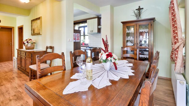 A dining room with a wooden table set for four, surrounded by chairs. A vase with flowers is on the table, and there is a cabinet with glass doors to the right.