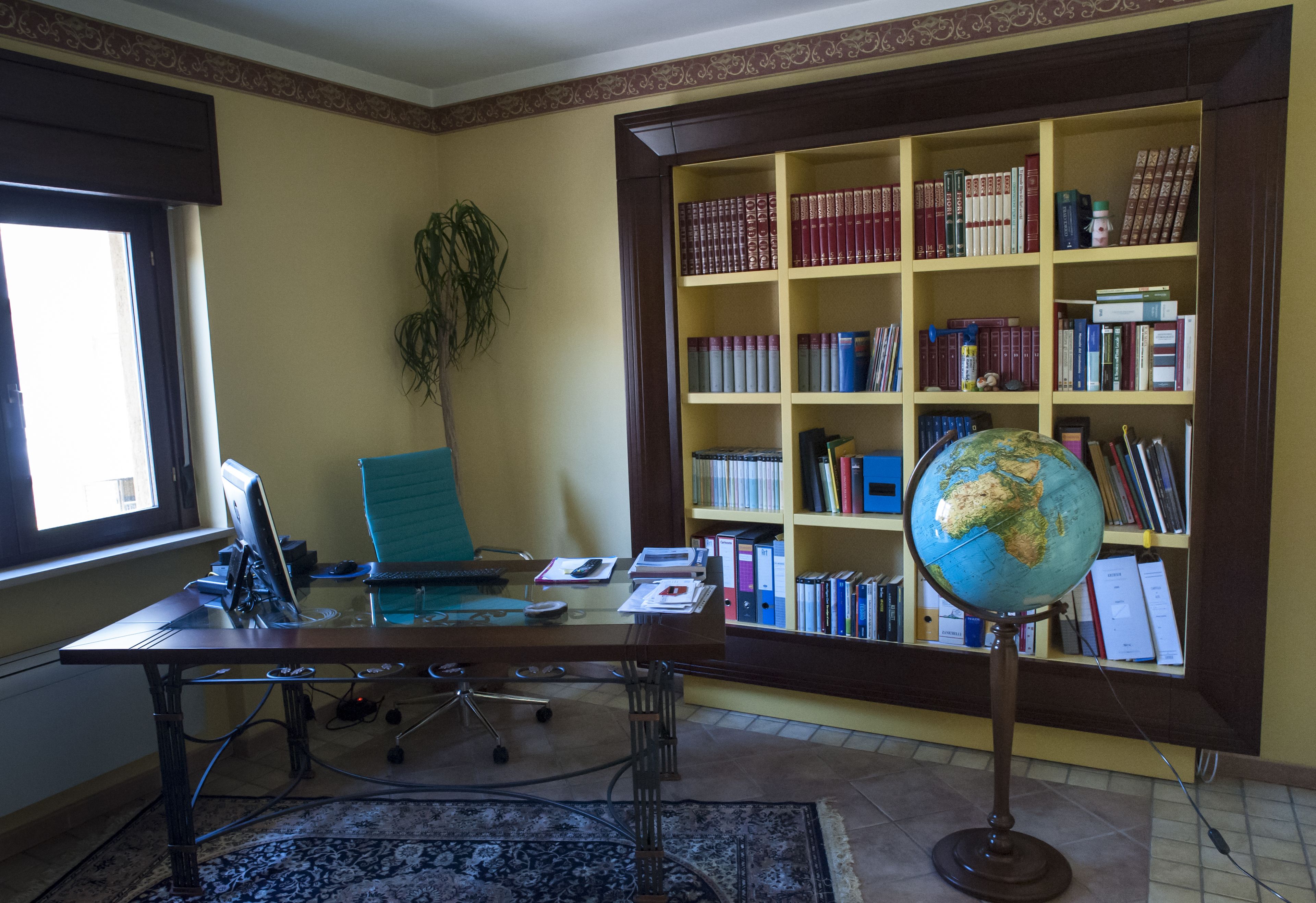 A study room with a desk, chair, bookshelf, globe, and a potted plant.
