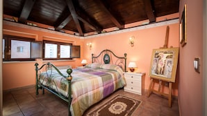 A bedroom with a bed, bedside lamps, a dresser, a window, and an easel with a painting.
